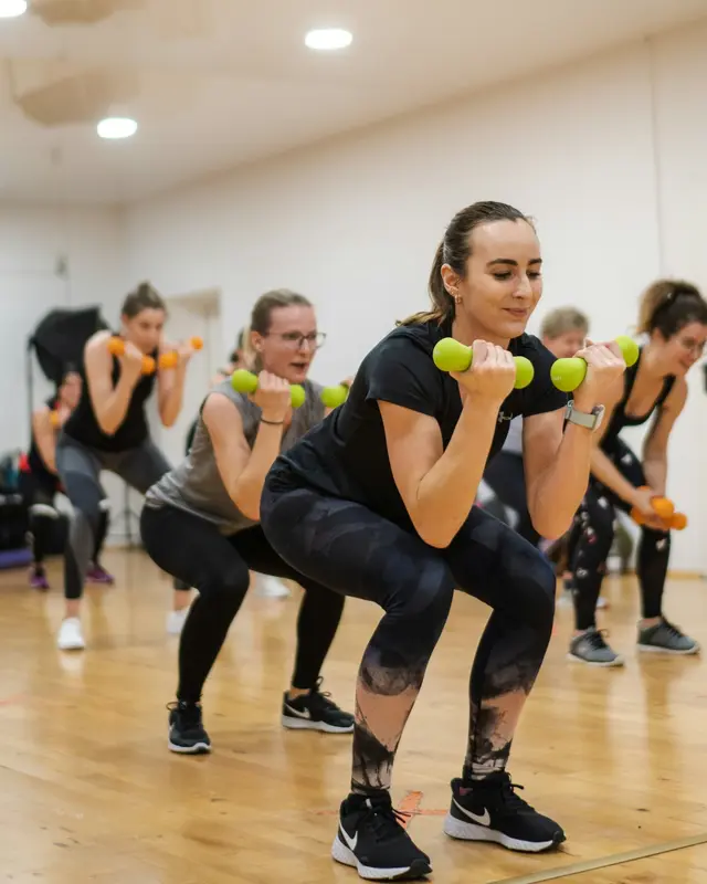 Un grupo de mujeres hace sentadillas con mancuernas en una clase